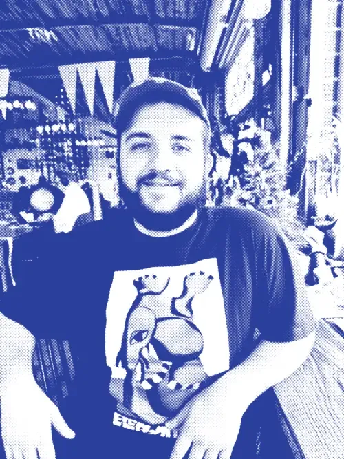 A picture of Reid sitting at a table in a cafe. He is wearing a light brown baseball cap and a black shirt with the words 'elephant gym' on the front